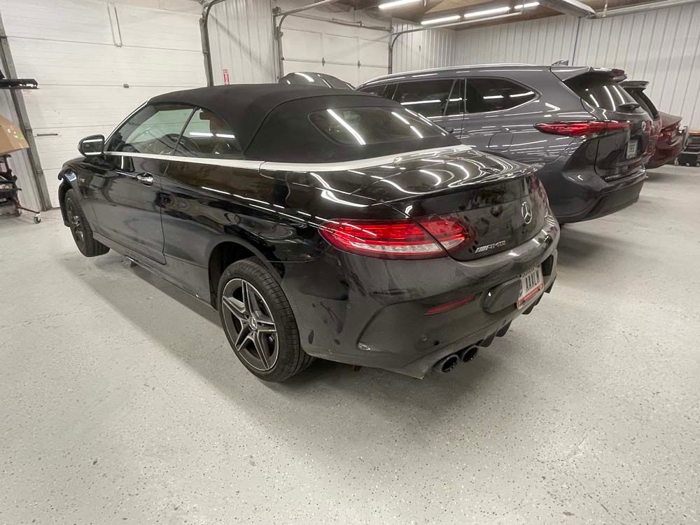 A black convertible is parked in a garage next to another car.