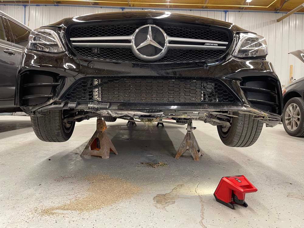 A black mercedes benz is sitting on jack stands in a garage.