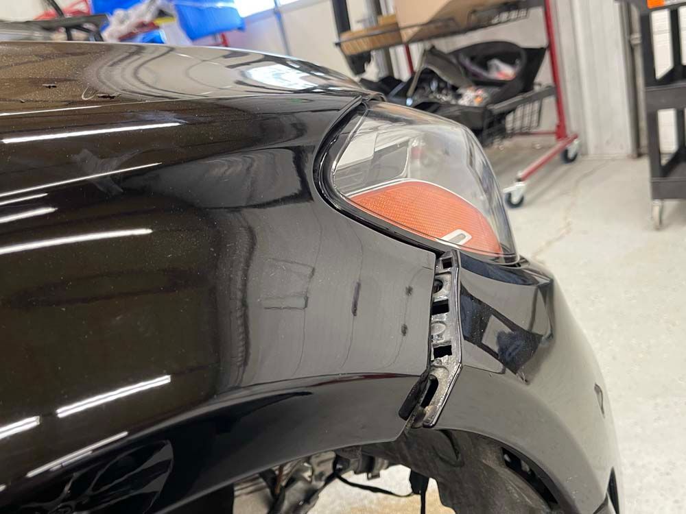 A black car with a broken bumper is sitting in a garage.