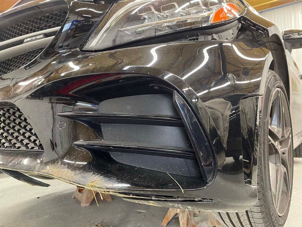 A black car with a damaged bumper is parked in a garage.