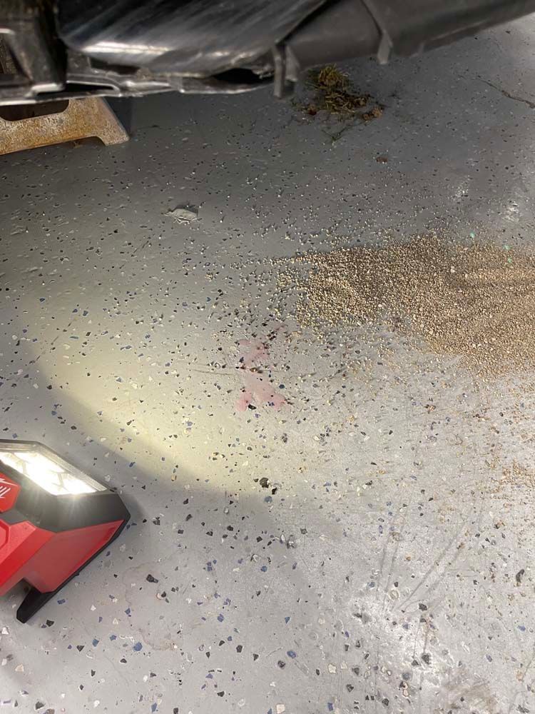 A red and black flashlight is sitting on the floor next to a car.