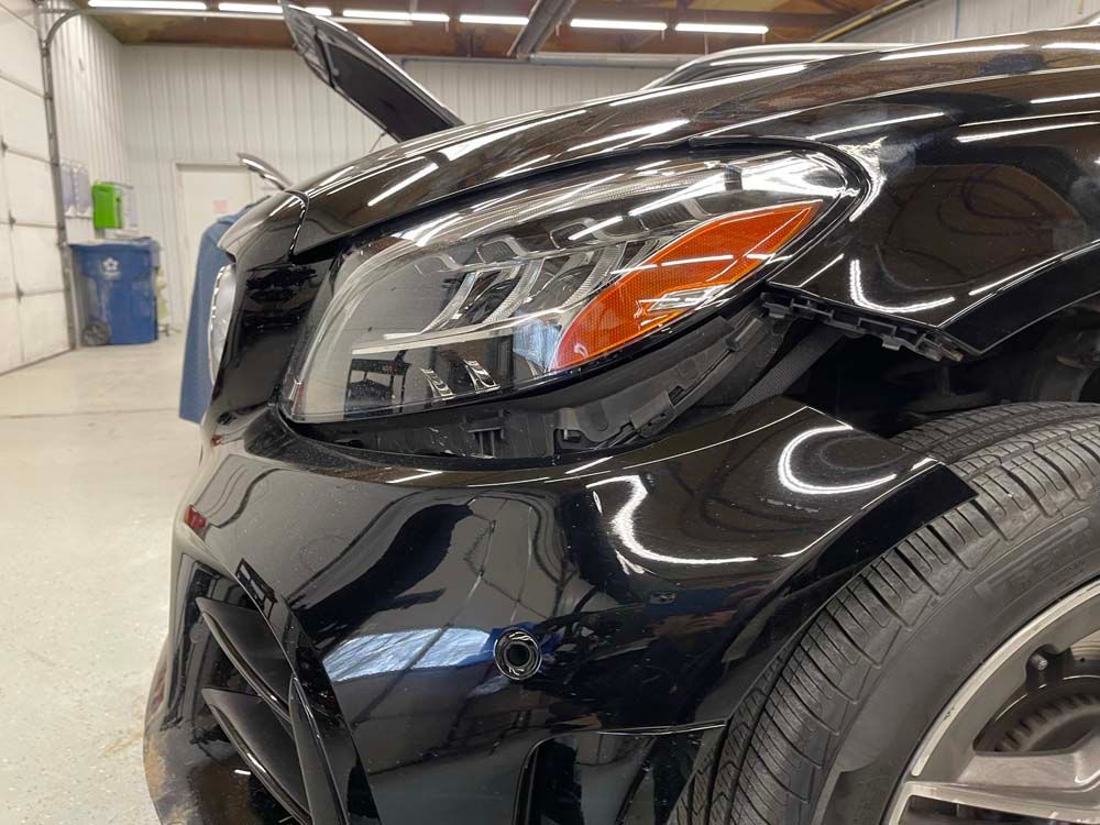 A black car with a damaged bumper is parked in a garage.