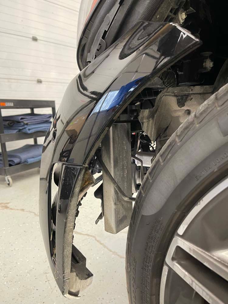 A close up of a car bumper and tire in a garage.