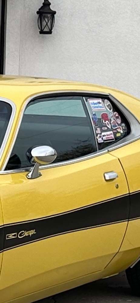 A yellow dodge challenger is parked in front of a building.