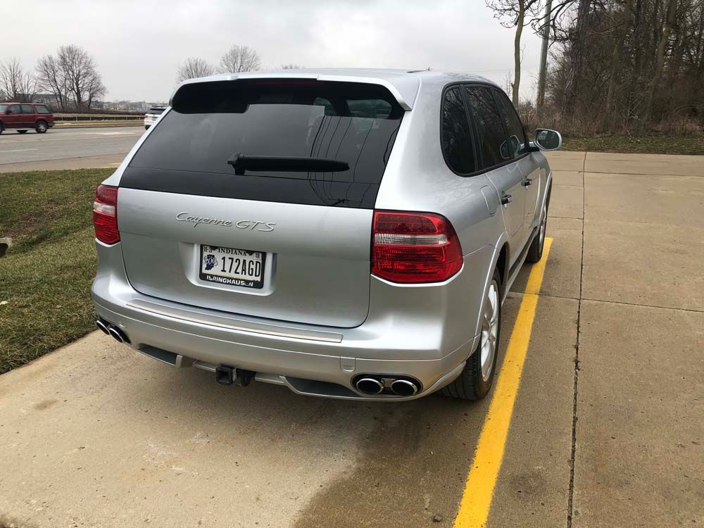 A silver porsche cayenne is parked in a parking lot.