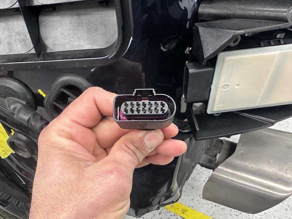 A person is holding a connector in their hand in front of a car.