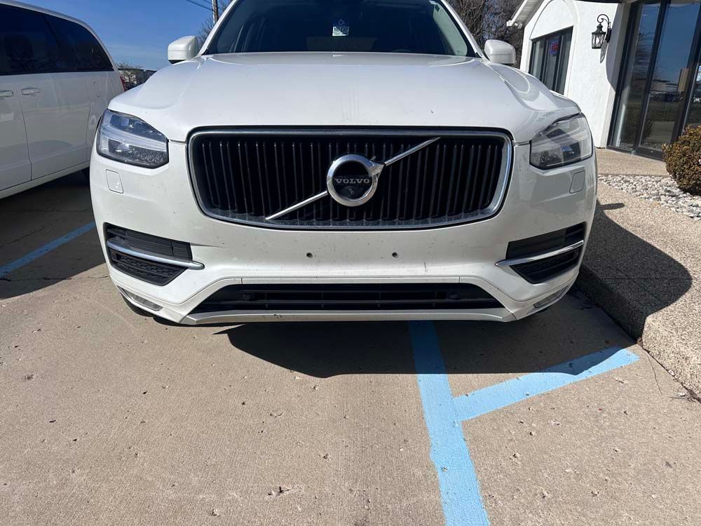 A white volvo xc90 is parked in a parking lot.