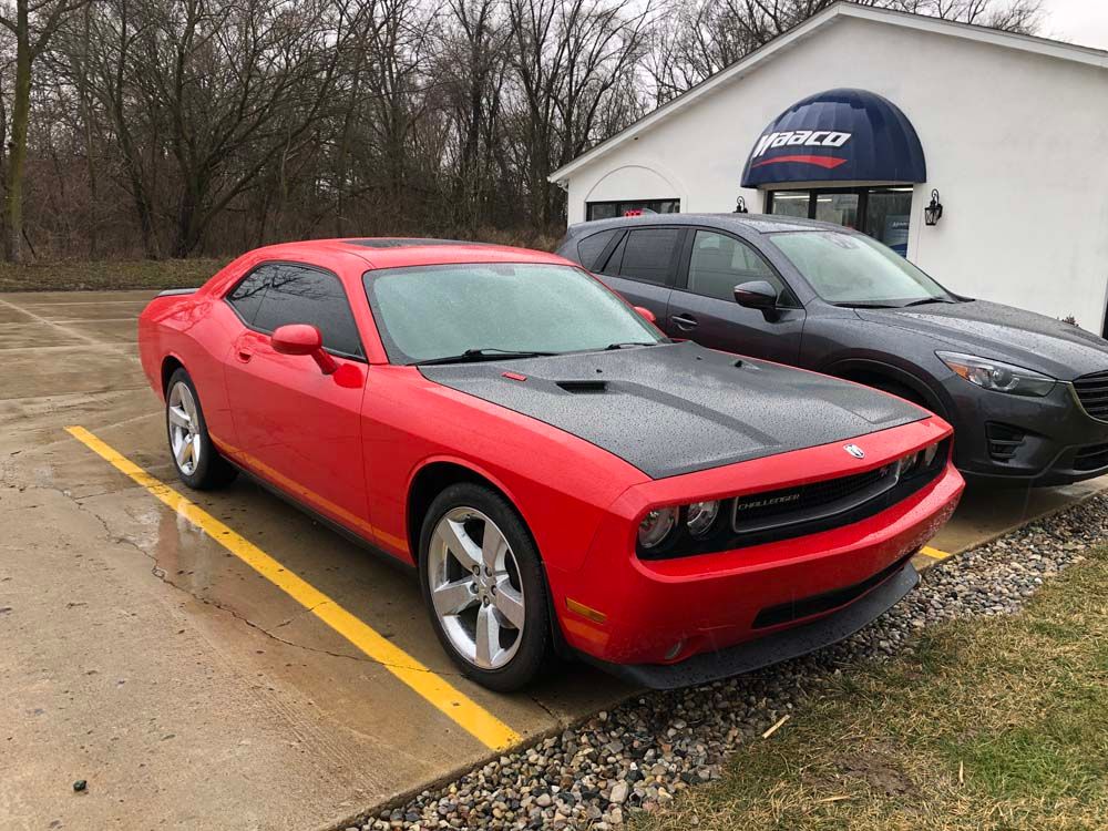 Red Dodge Challenger with black hood stripes parked outside a business.