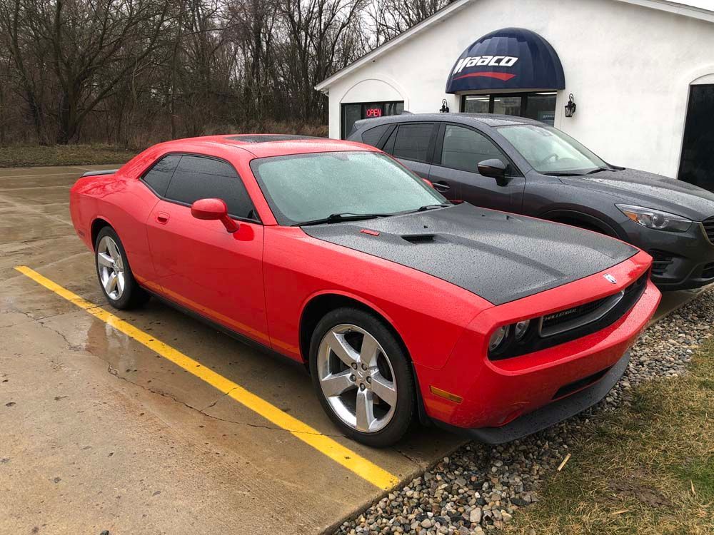 A red dodge challenger is parked in a parking lot next to a black car.