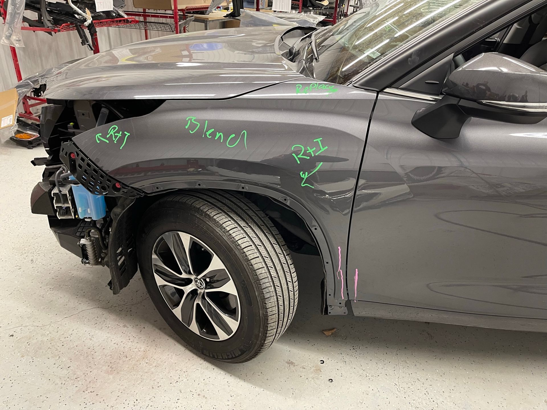 A gray car with a damaged fender is sitting in a garage.