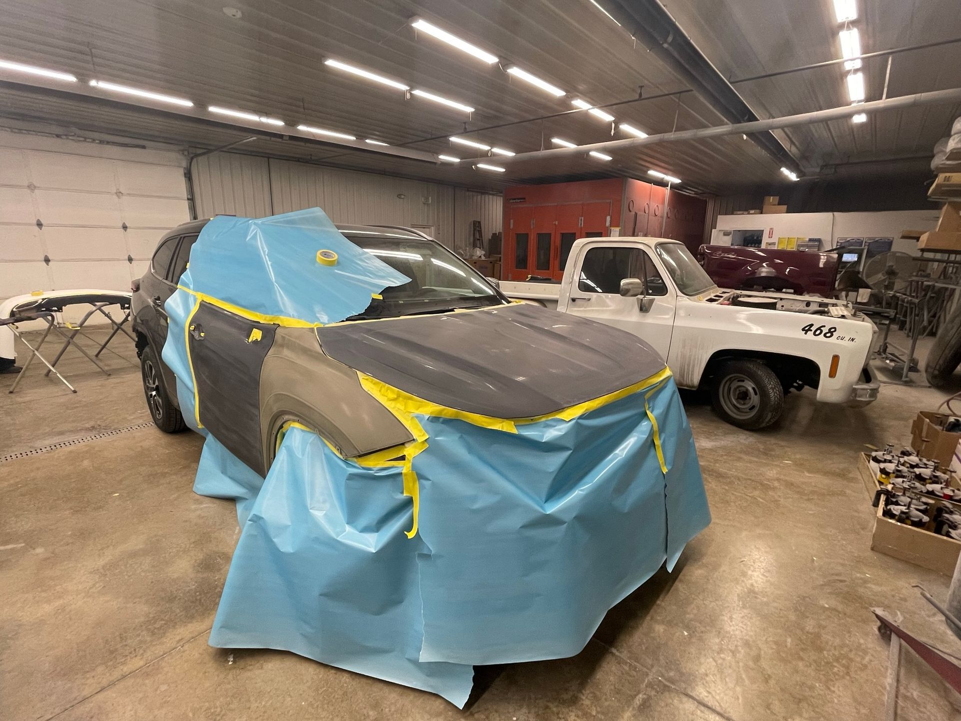 A car is covered in blue plastic in a garage.