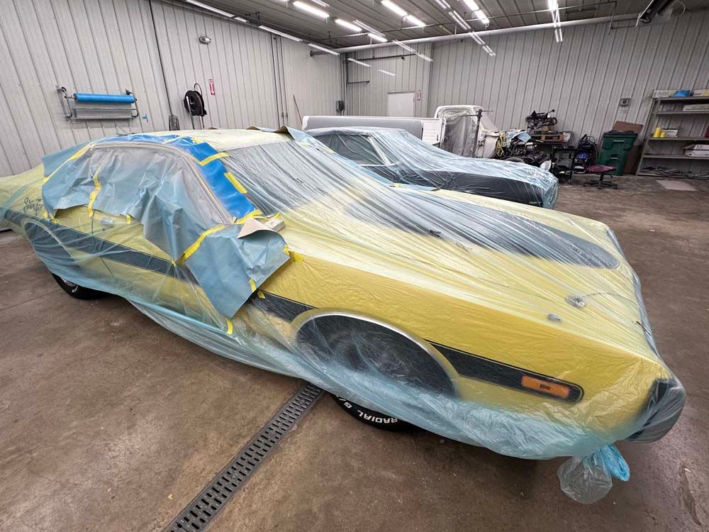 A yellow car is wrapped in plastic in a garage.