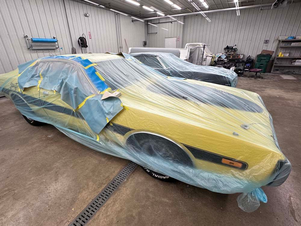 A yellow car is wrapped in plastic in a garage.