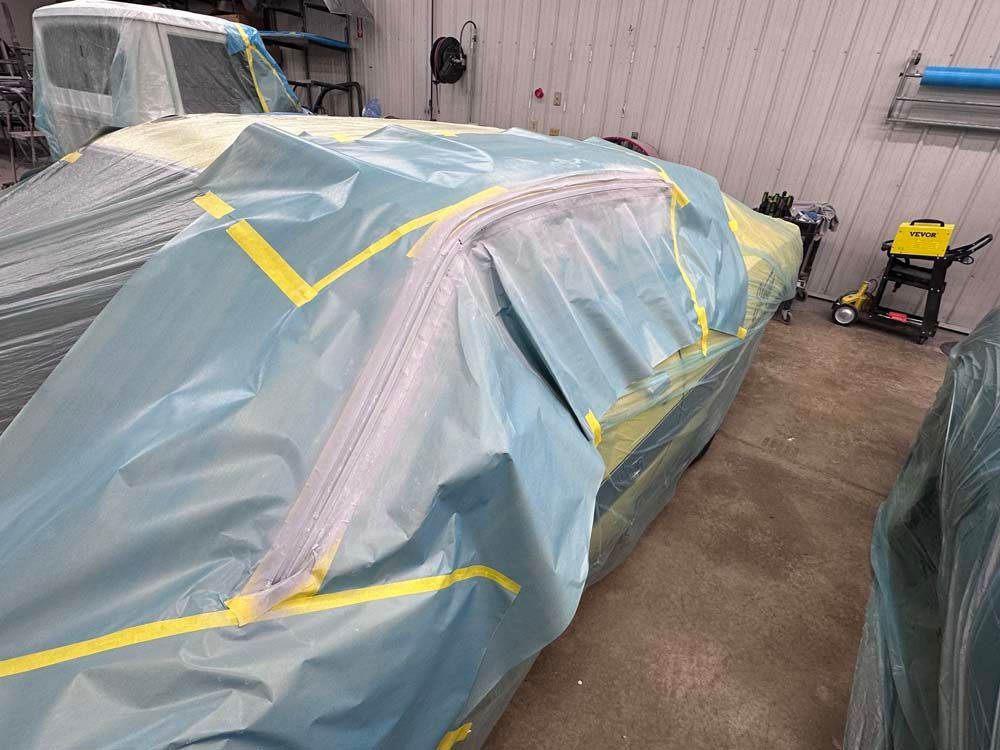 A car is covered in plastic and tape in a garage.