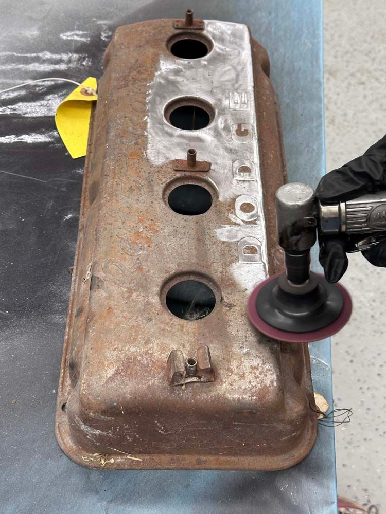 A person is polishing a rusty valve cover with a sander.