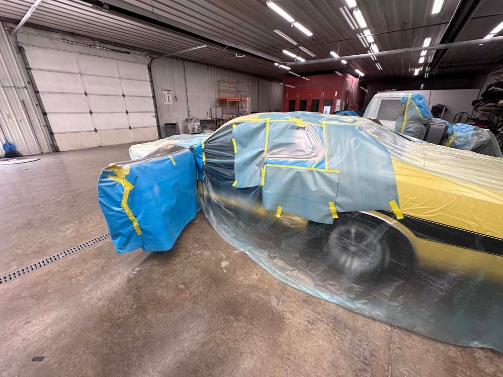 A yellow car is covered in plastic wrap in a garage.