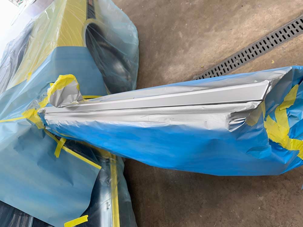 A blue bag with yellow tape on it is sitting on the ground next to a drain.