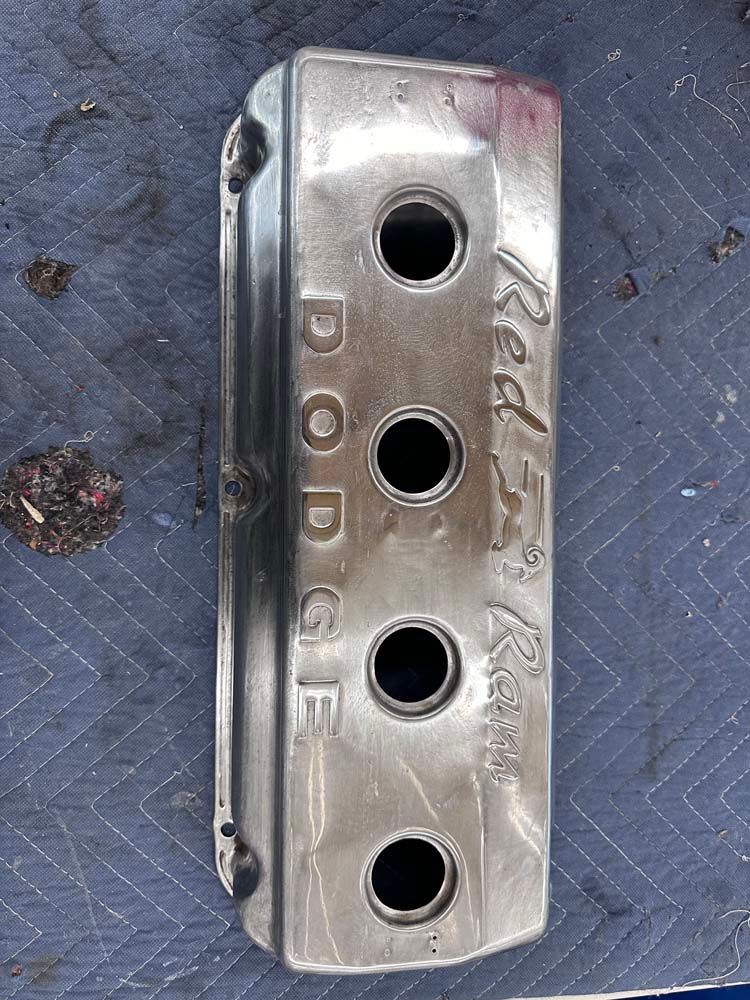 A stainless steel valve cover for a dodge engine is sitting on a table.