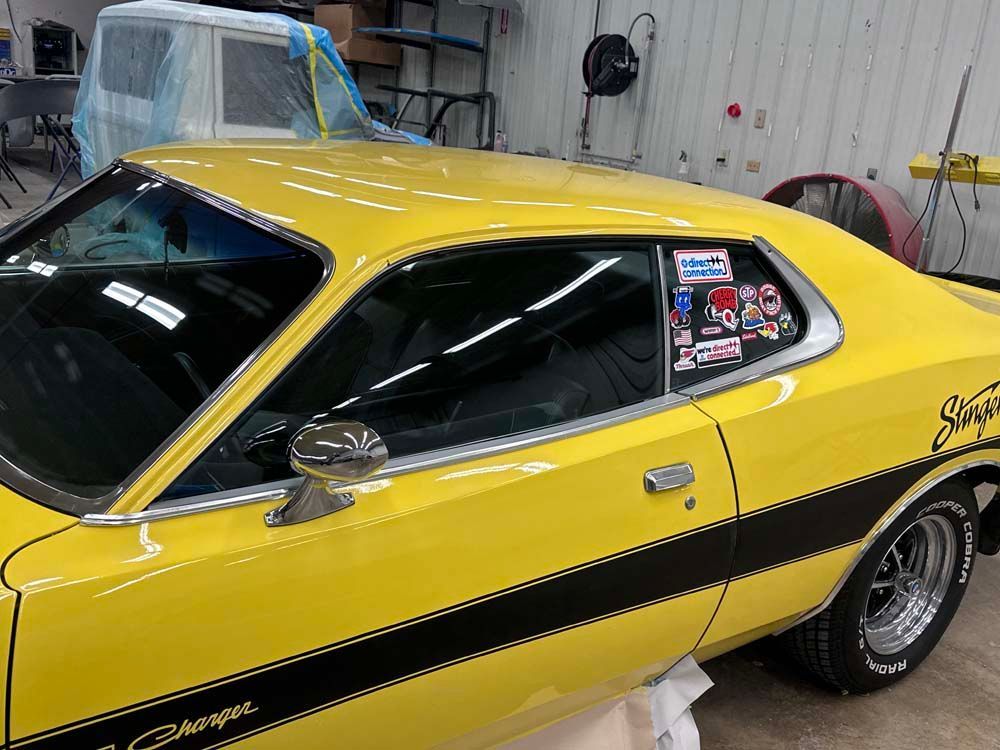 Yellow classic Charger with black racing stripe and chrome details, inside a garage.