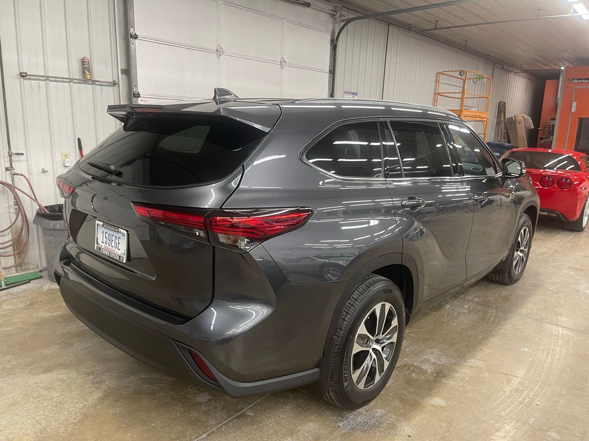 A gray toyota highlander is parked in a garage next to a red car.