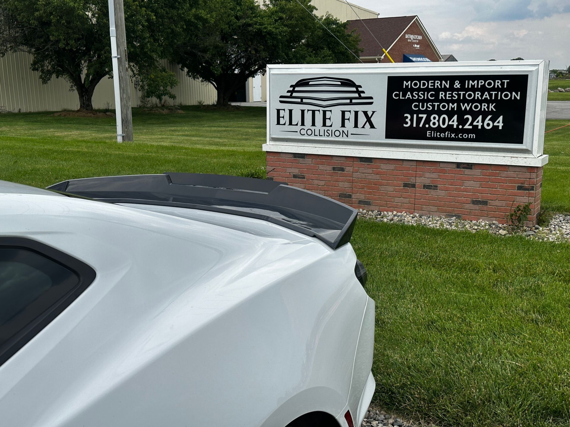 White car with spoiler in front of a sign for 