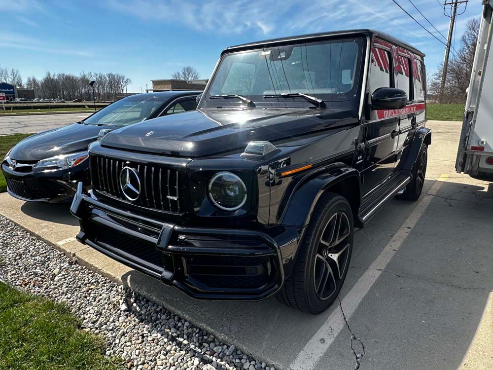 A black mercedes benz g63 amg is parked in a parking lot next to a black car.