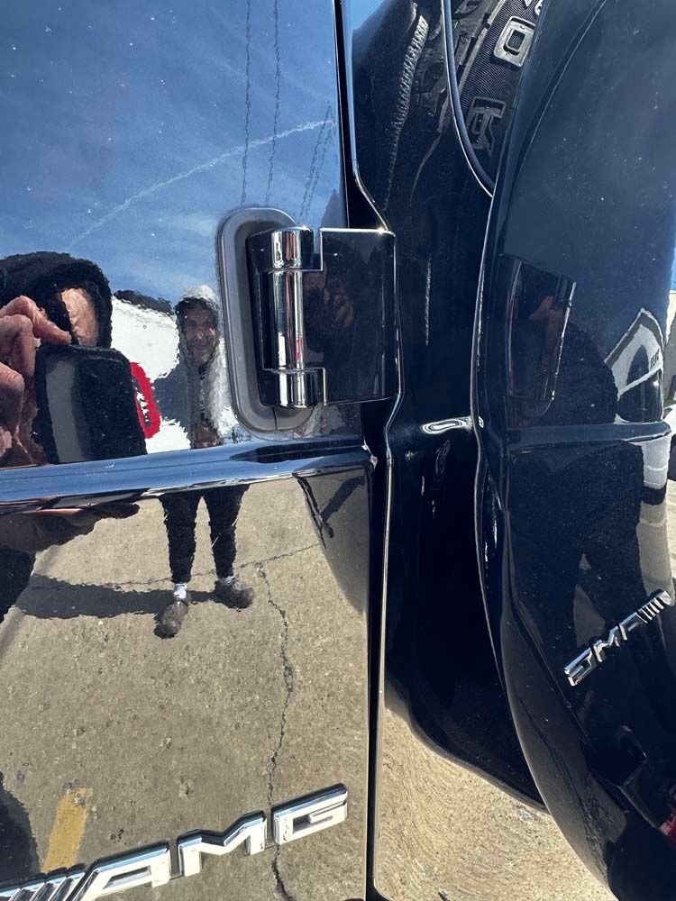 A man is taking a picture of himself in the mirror of a black amg car.