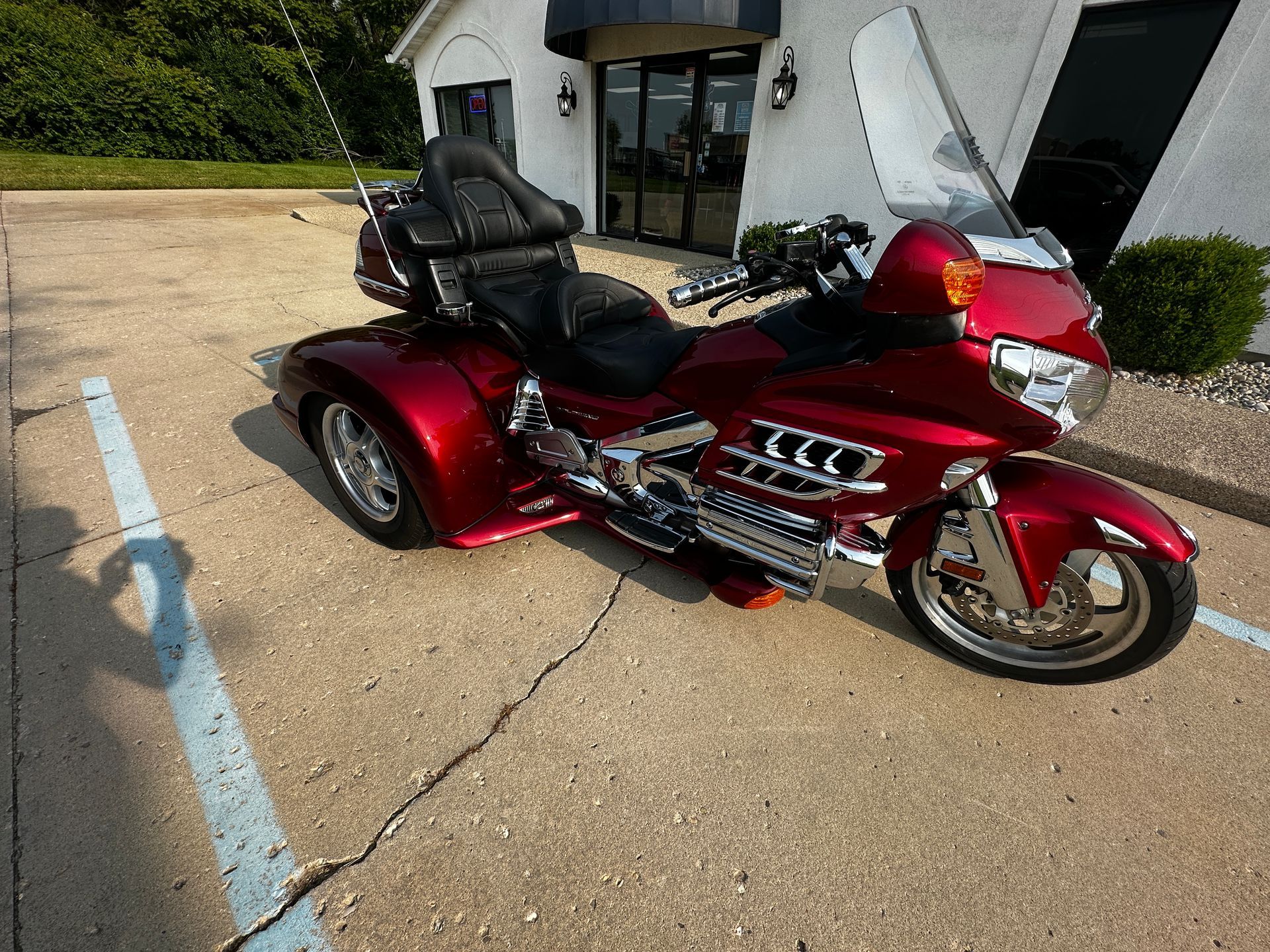 A red three-wheeled motorcycle parked in a concrete lot in front of a building.