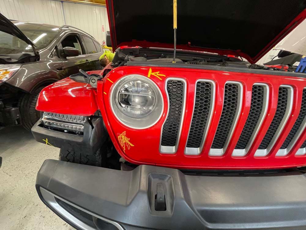 A red jeep with the hood open is sitting in a garage.