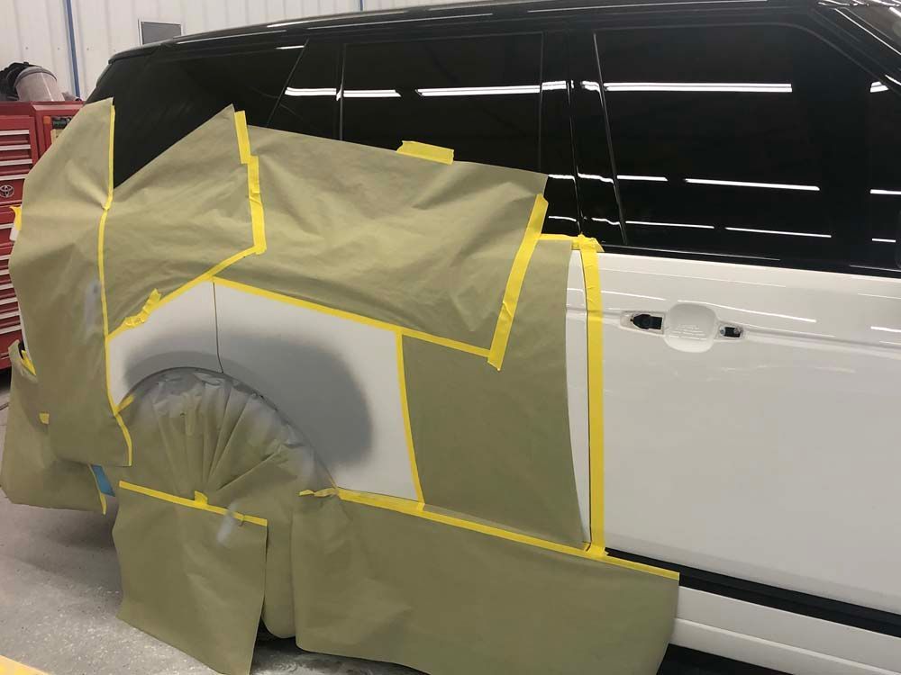 A white van is covered in plastic and tape in a garage.