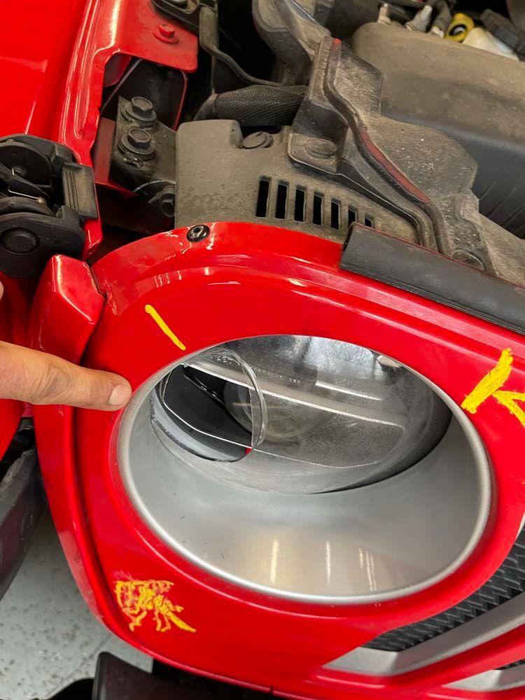 A person is pointing at the headlight of a red car.