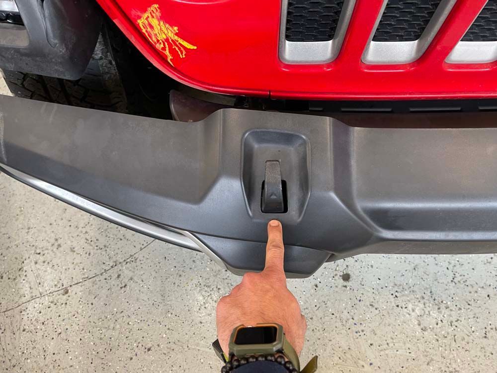 A person is pointing at the bumper of a red jeep.