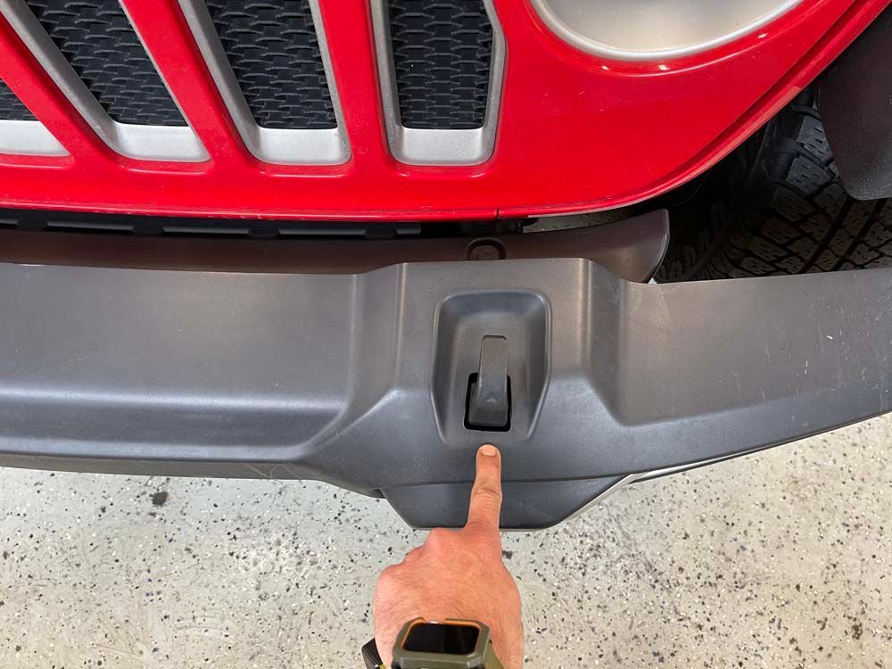 A person is pointing at the front bumper of a red jeep.