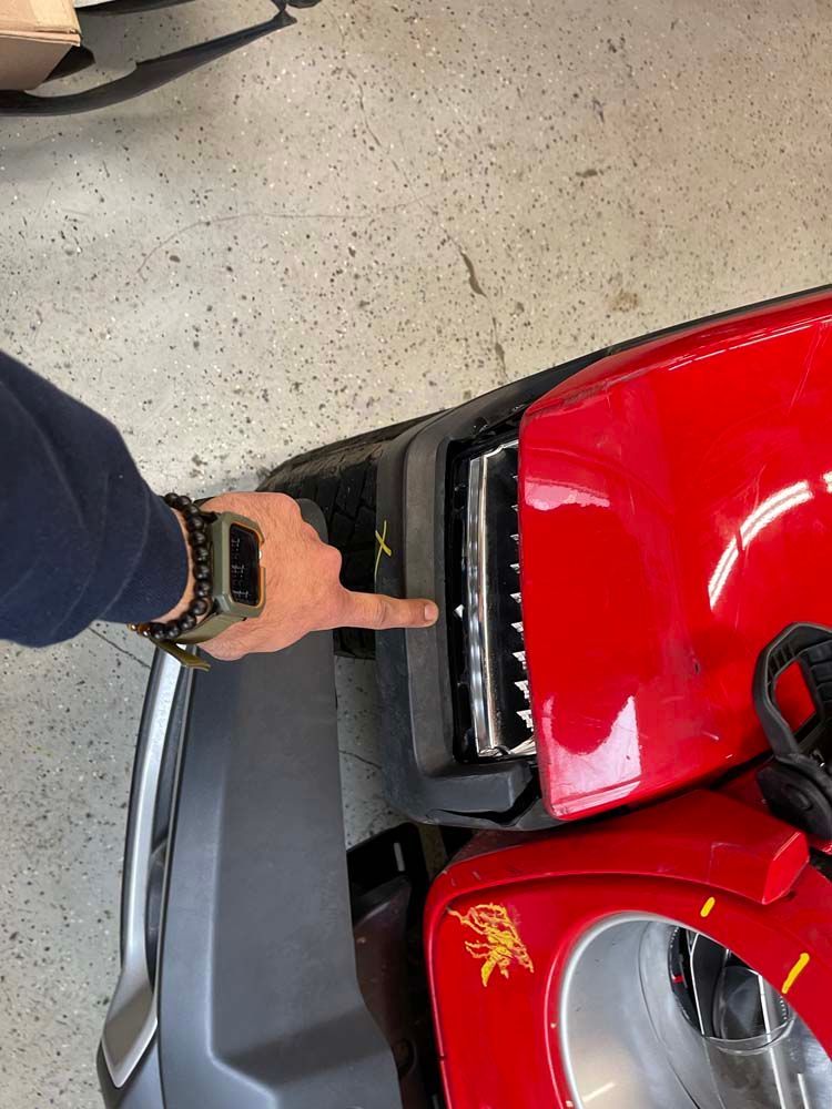 A person is pointing at the front bumper of a red jeep.