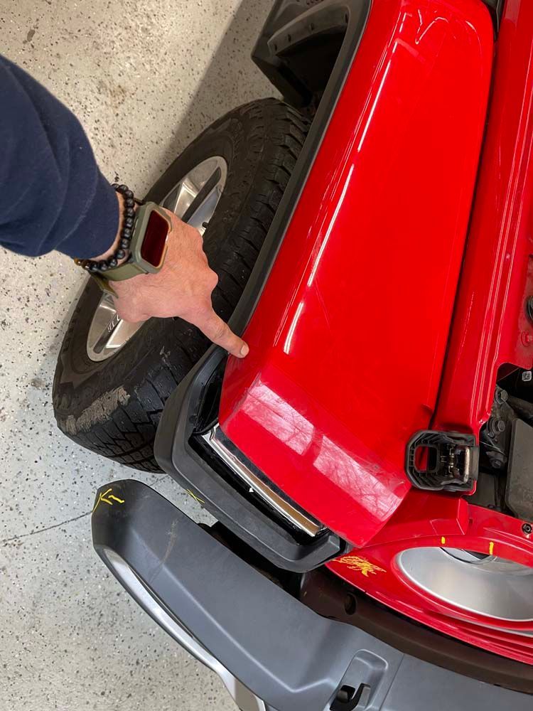 A person is pointing at the front of a red jeep.