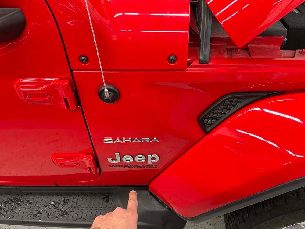 A person is pointing at the side of a red jeep.