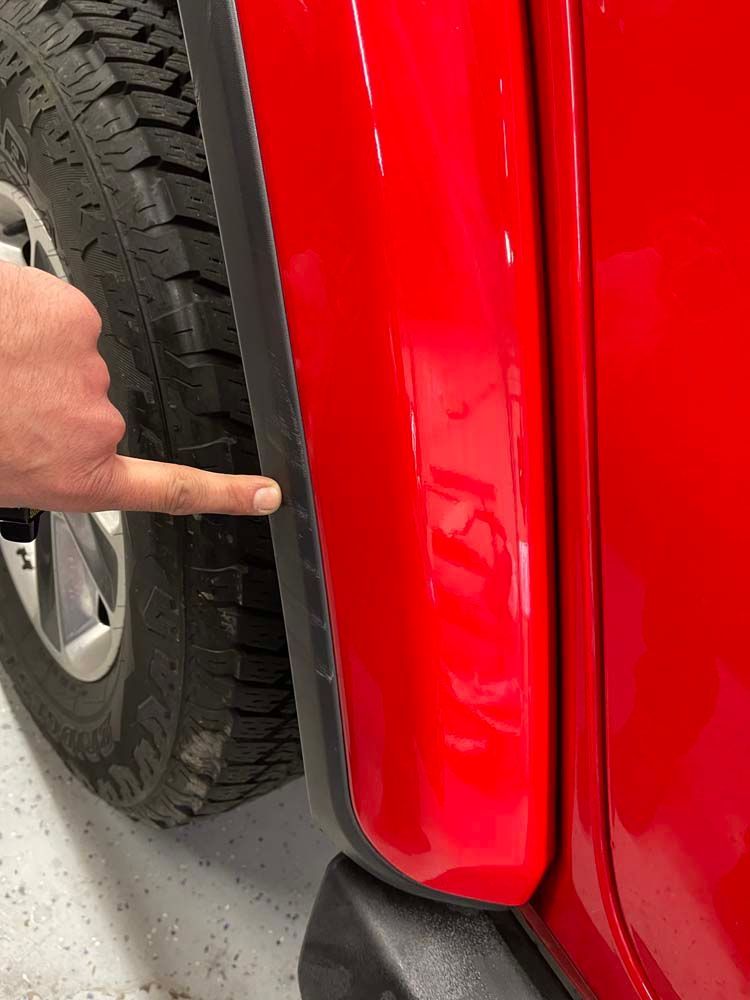 A person is pointing at the fender of a red car.