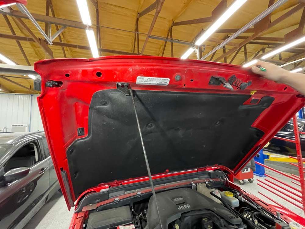 A person is opening the hood of a red jeep in a garage.
