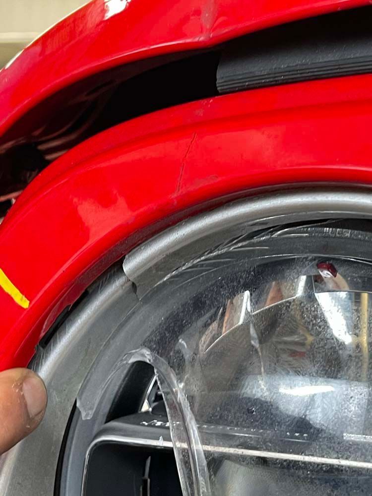 A person is holding the headlight of a red car.