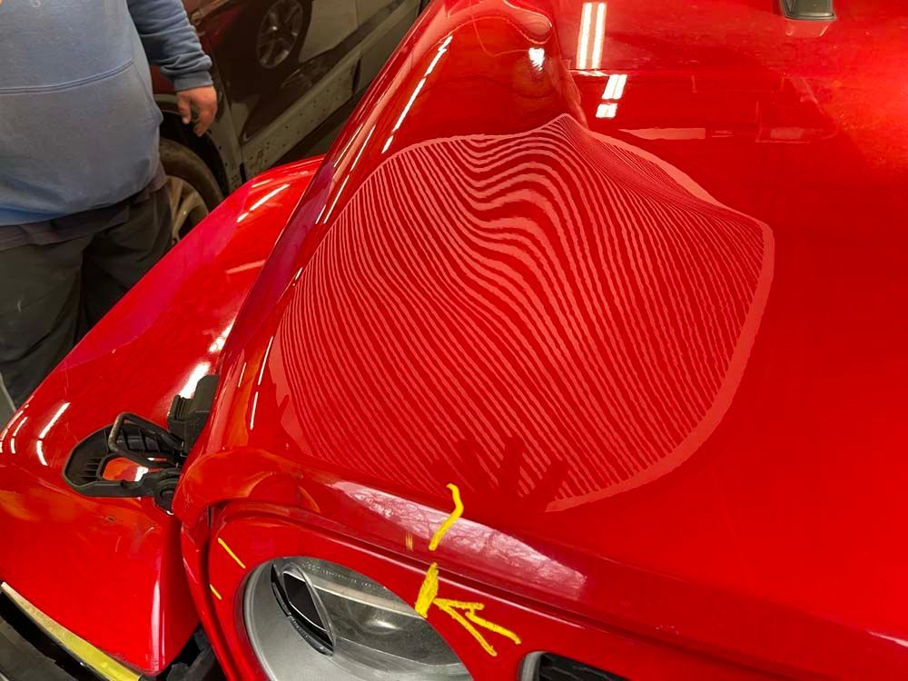 A man is standing next to a red car with a yellow x on it