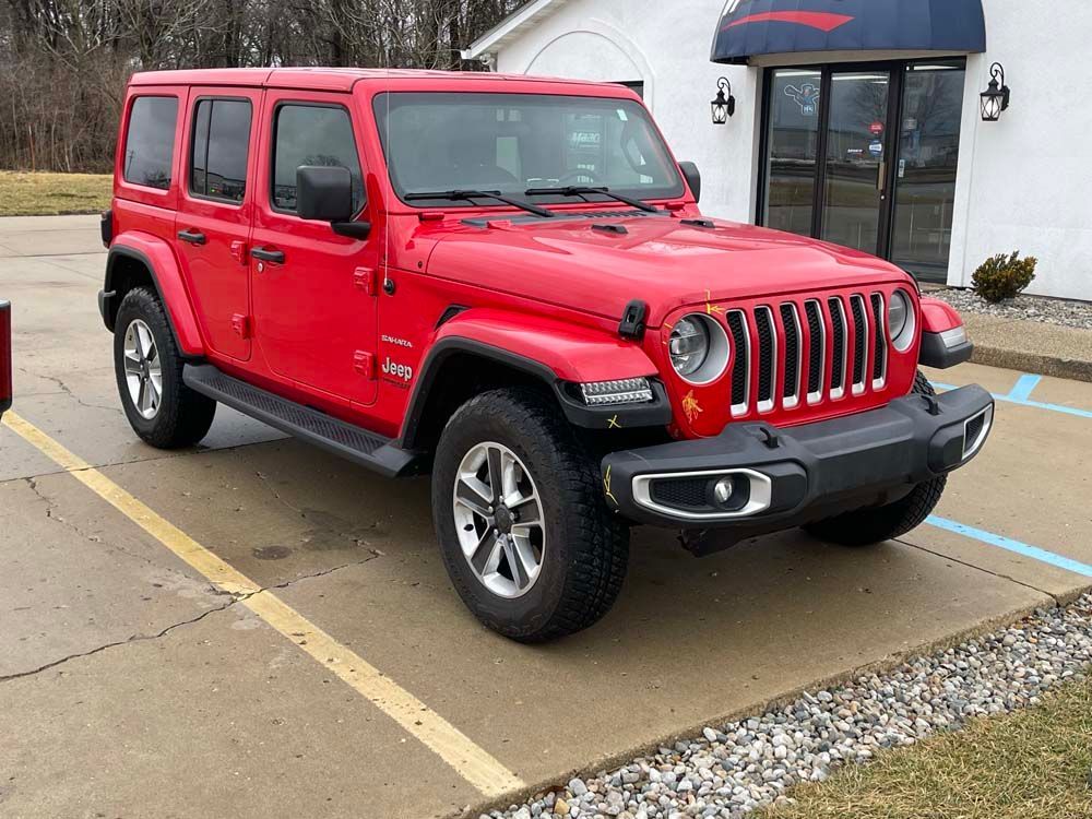 A red jeep wrangler is parked in a parking lot in front of a building.