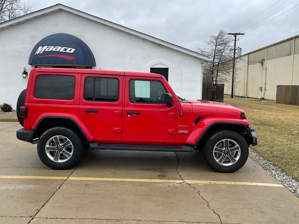 A red jeep wrangler is parked in front of a building.