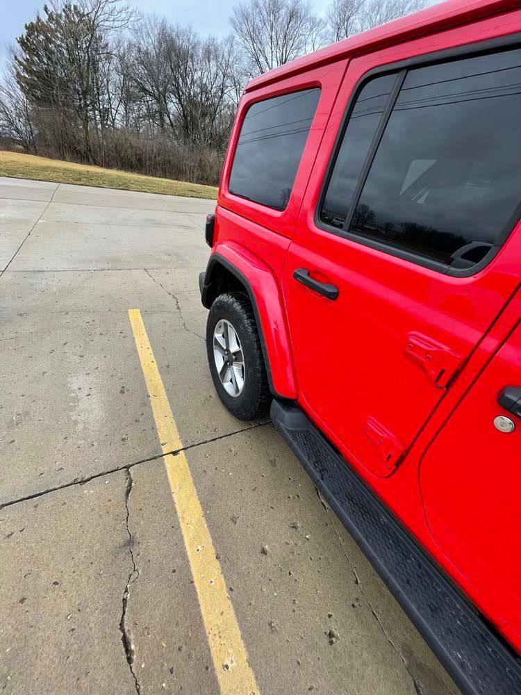 A red jeep is parked in a parking lot next to a yellow line.