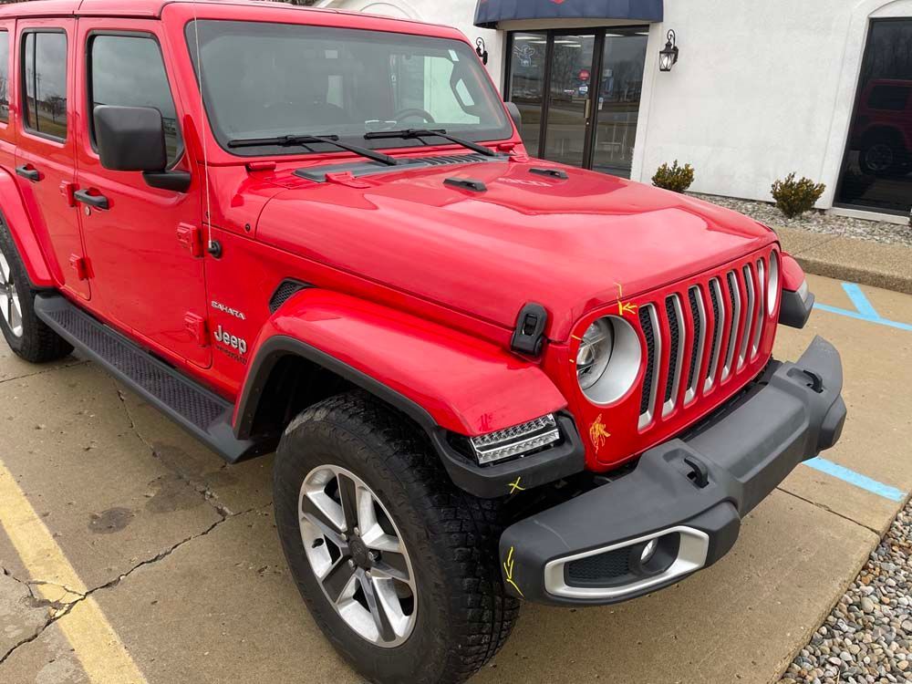 Red Jeep Wrangler parked in front of a building, on a paved surface.