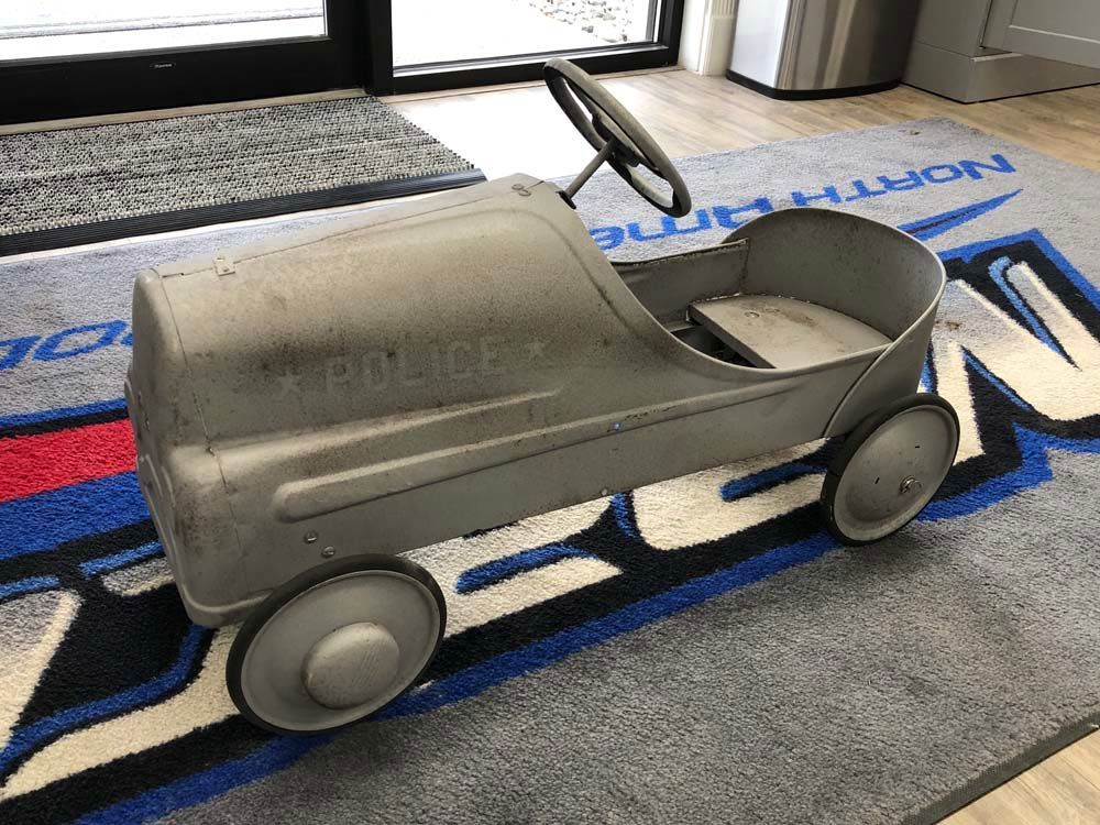 A gray pedal car is sitting on a blue and white rug.