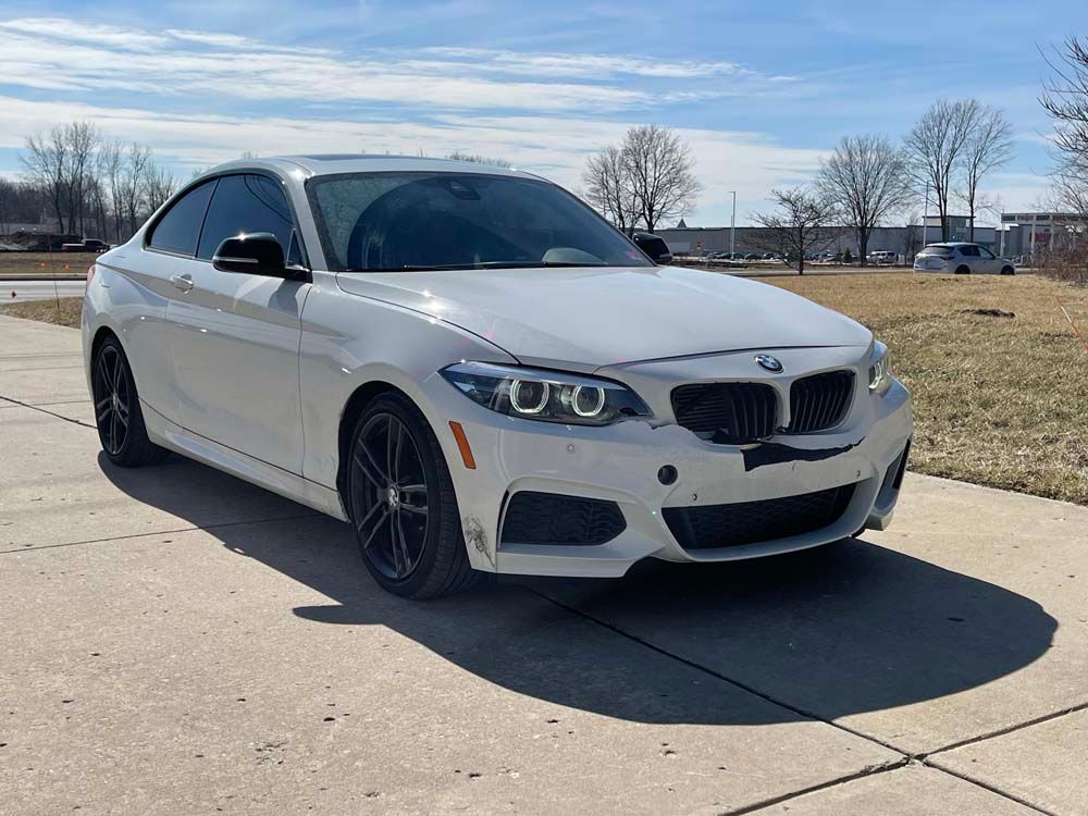 A white bmw 2 series coupe is parked on a sidewalk.
