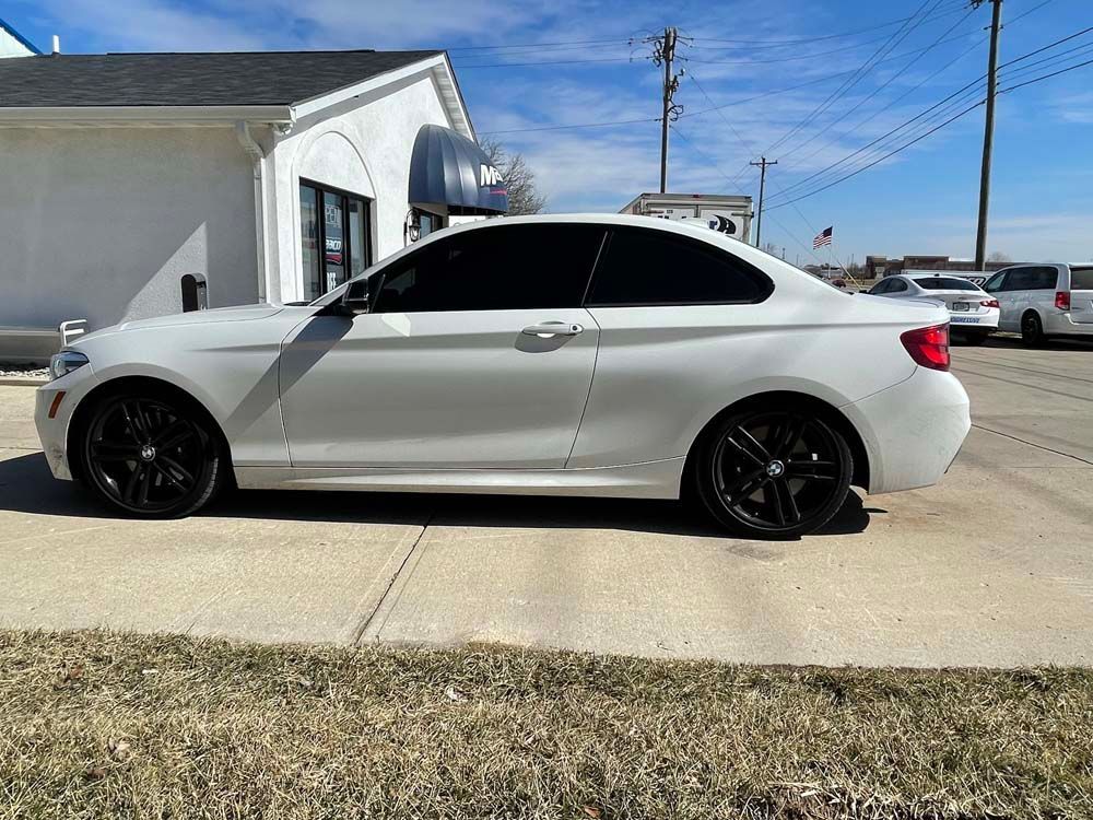 A white bmw is parked on the side of the road in front of a building.