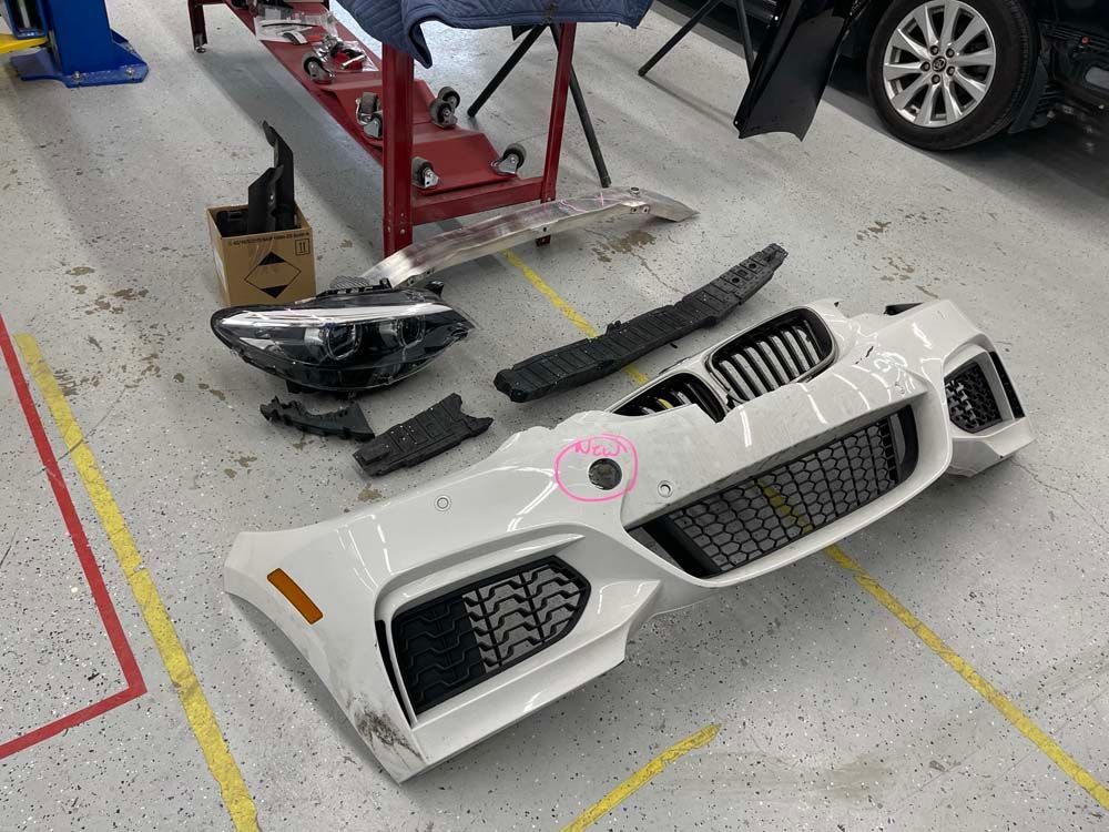 A white car bumper is sitting on the floor in a garage.