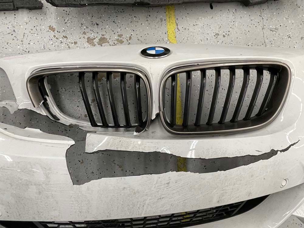 The front grille of a white bmw is damaged.