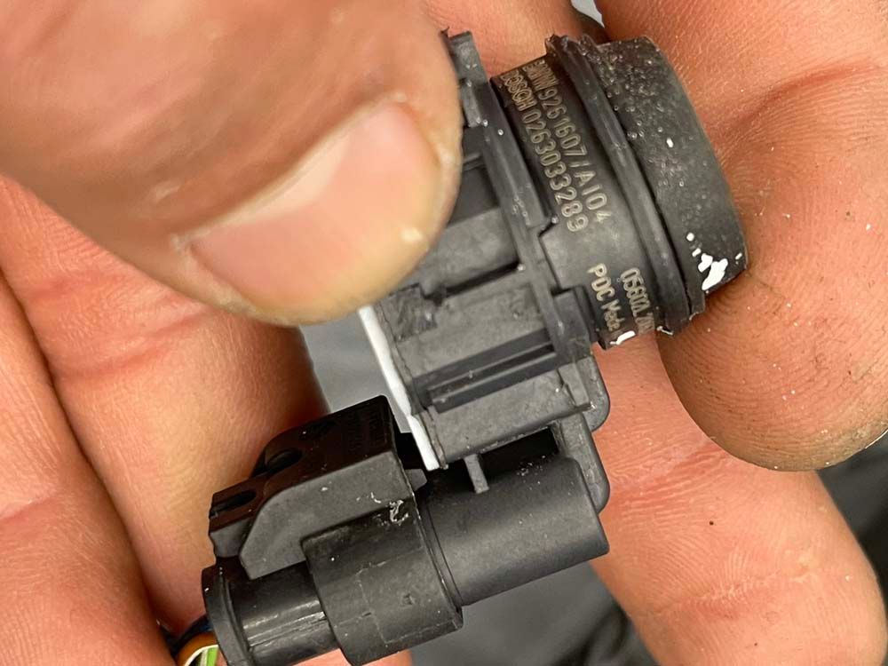 A person is holding a black connector in their hand.